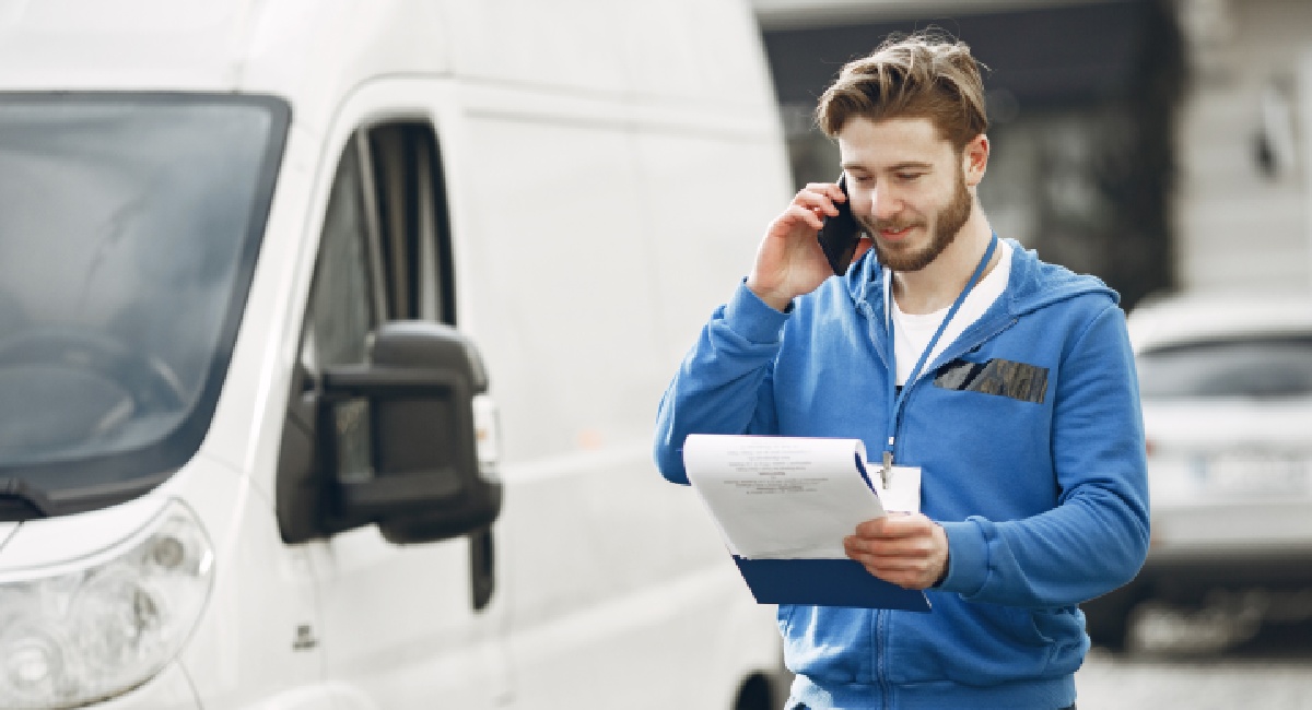 addetto alla logistica internazionale che consulta un block notes sorridendo per i vantaggi offerti dai trasporti Just In Time