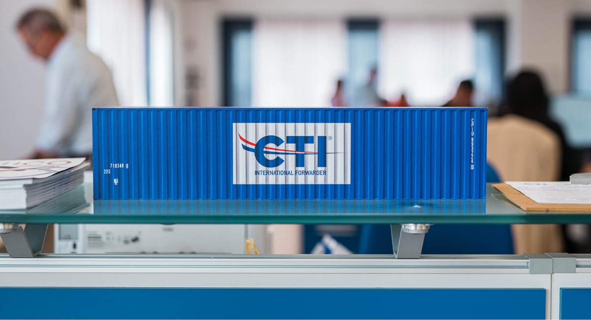 immagine di una miniatura di container azzurro con il logo CTI, sul retro, sfocato, l'ufficio amministrativo di CTI, partner logistico outsourching.